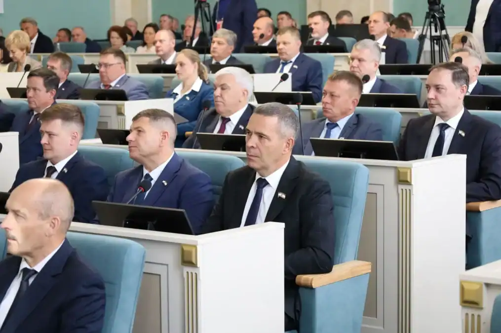 Участники заседания сидят рядами за рабочими местами с мониторами.
