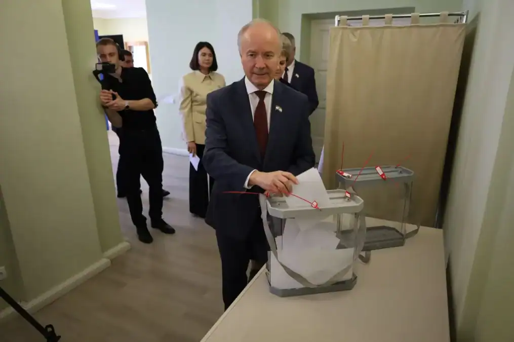 Мужчина опускает бюллетень в прозрачный ящик для голосования.