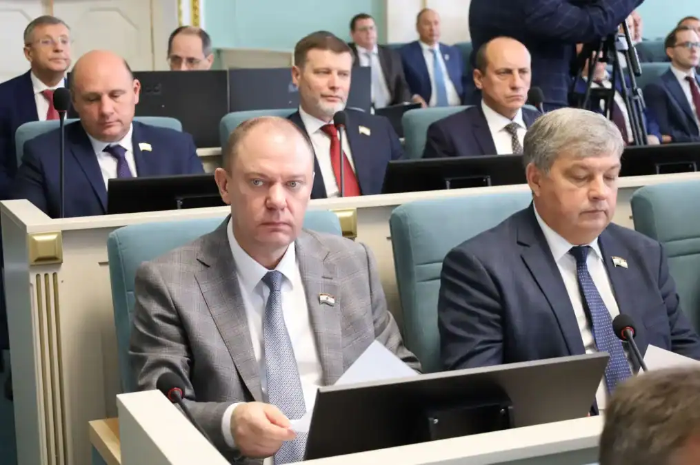 Депутаты сидят за рабочими местами с мониторами и документами.