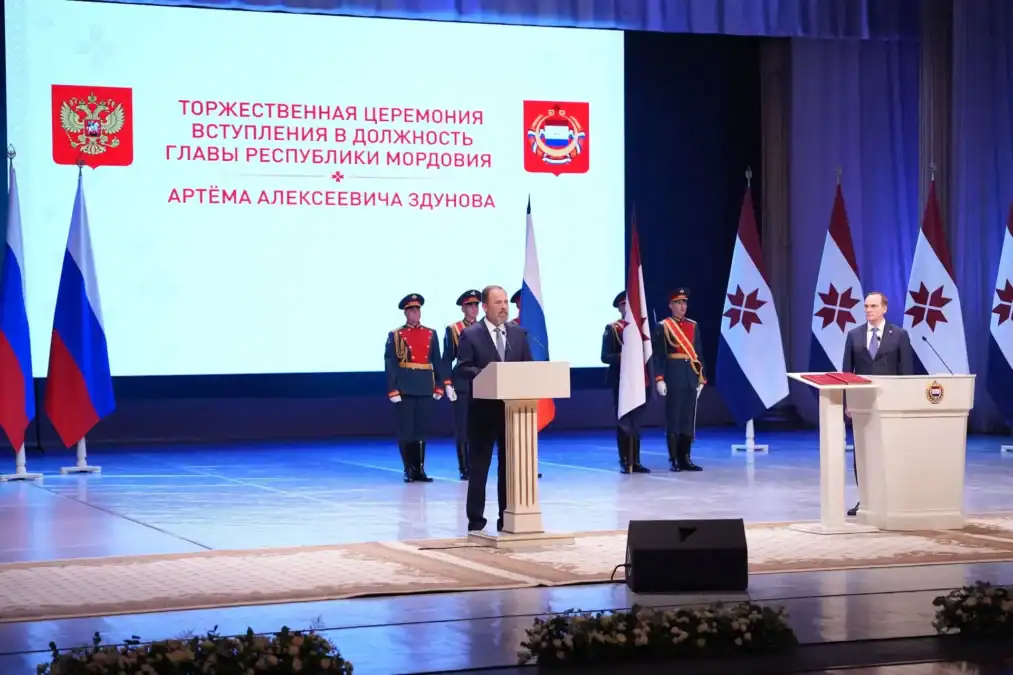 Два выступающих находятся у трибун на сцене перед экраном церемонии.