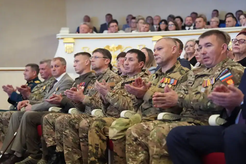 Мужчины в камуфляжной форме с наградами аплодируют в зрительном зале.