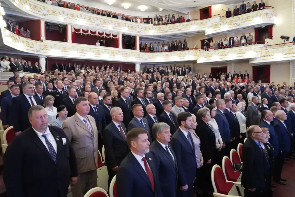 Участники торжественной церемонии стоят в заполненном зрительном зале.