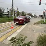 Бордовый седан стоит на пешеходном переходе рядом с сигнальным конусом.
