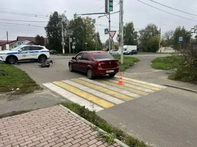 Бордовый седан у перехода, рядом видны служебный автомобиль и лежащий самокат.