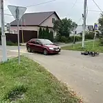 Бордовый седан и лежащий электросамокат находятся у перекрёстка с пешеходным переходом.