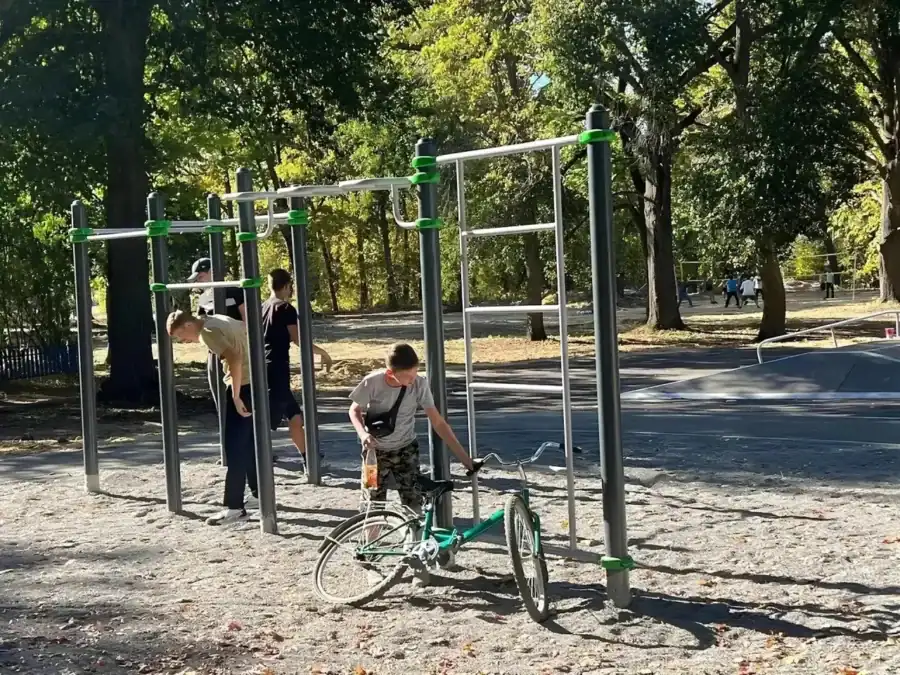 Подростки находятся у турников в парке, рядом стоит велосипед.