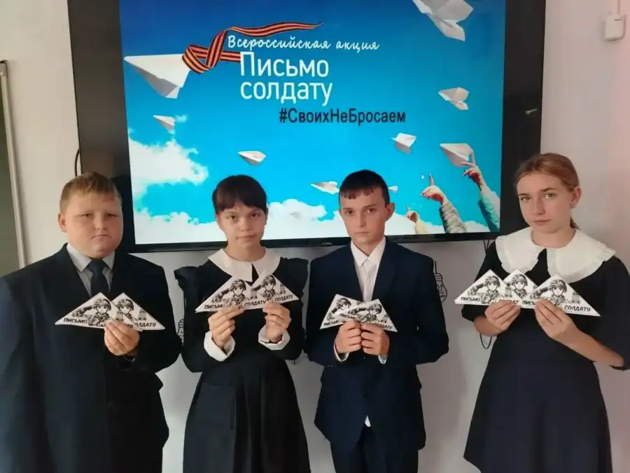 Четверо школьников показывают письма-треугольники перед экраном акции.