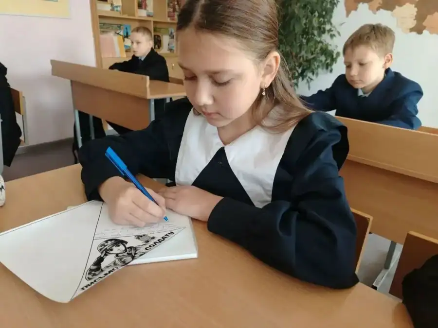 Школьница за партой пишет на листе, сложенном в виде письма-треугольника.