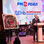 Мужчина выступает с трибуны на сцене перед оркестром.