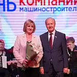 Женщина с букетом стоит на сцене рядом с мужчиной в костюме.