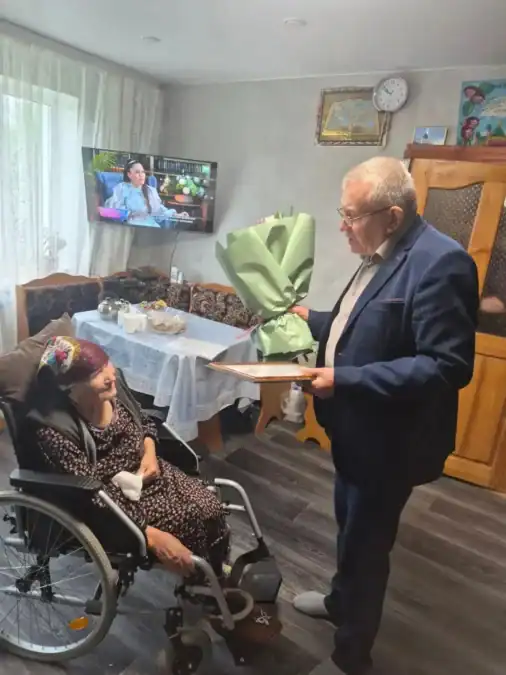 Мужчина вручает женщине в инвалидной коляске букет в домашней комнате.