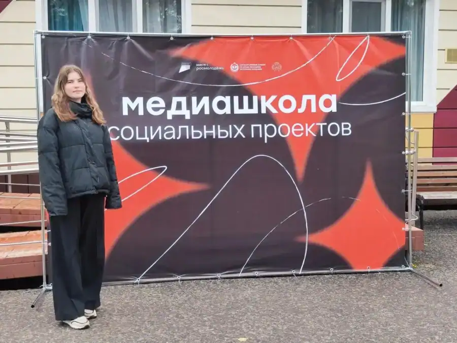 Девушка стоит рядом с баннером медиашколы социальных проектов.