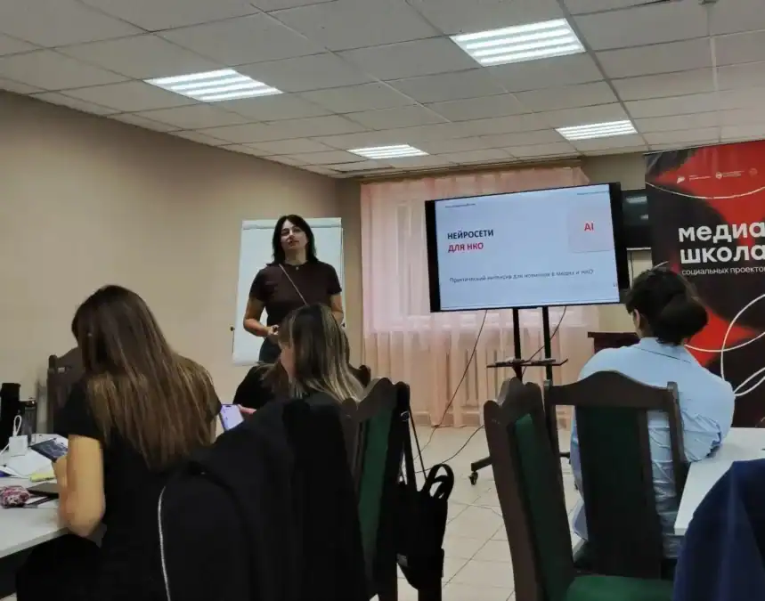 Участники сидят в аудитории и слушают спикера у презентационного экрана.