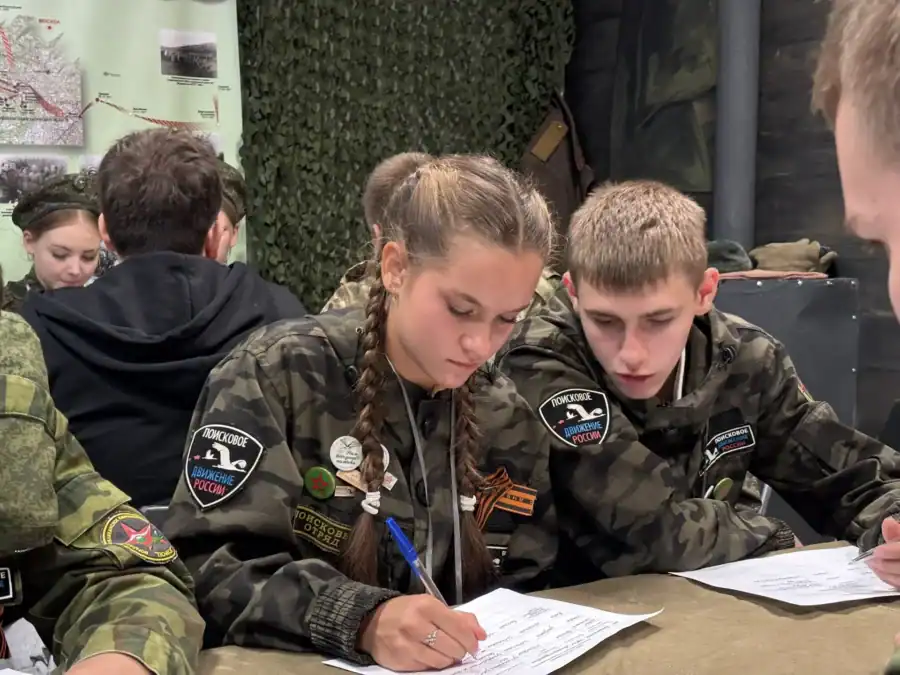 Двое участников поискового движения заполняют листы за столом.