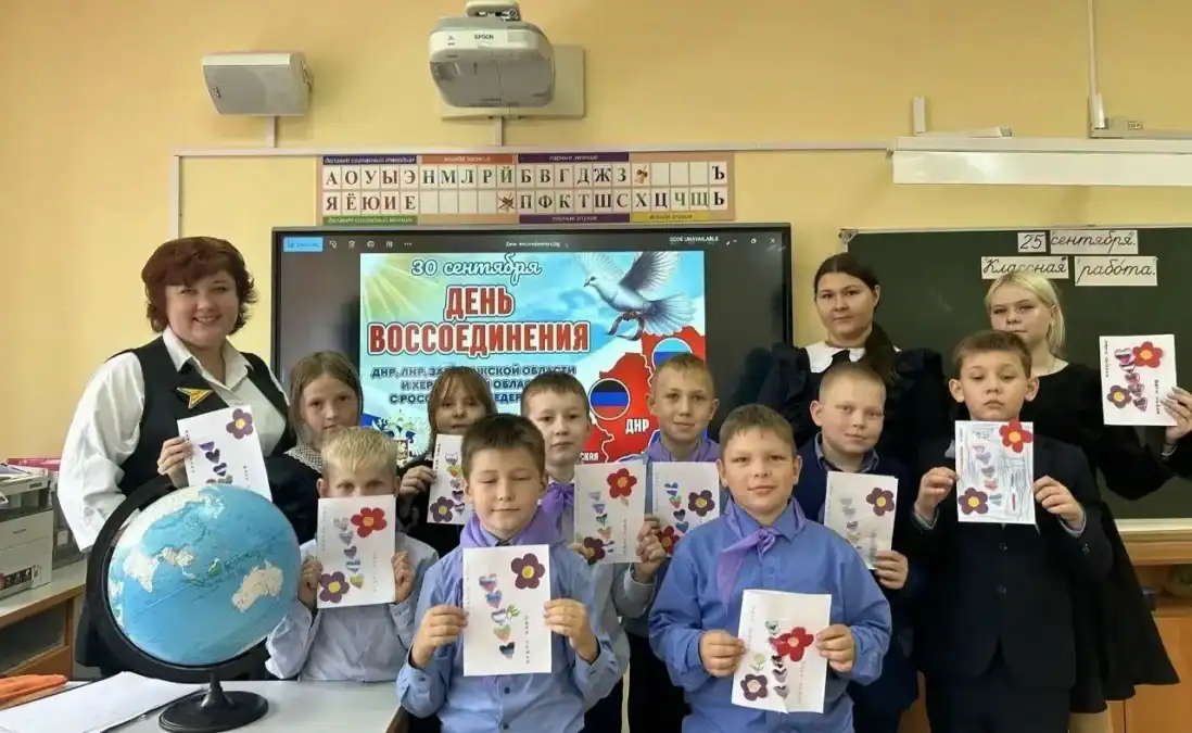 Школьники держат сделанные открытки с цветами перед экраном с тематической презентацией.