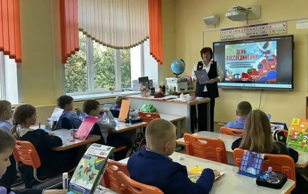 Педагог показывает материал у экрана, ученики сидят за партами в классе.
