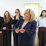Женщина перерезает красную ленту в окружении студентов.