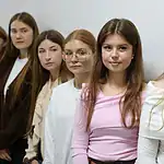 Несколько студенток стоят у светлой стены в университетском помещении.