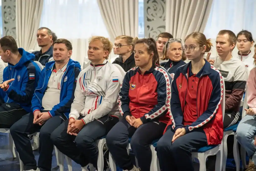 Спортсмены в экипировке сидят в зале перед соревнованиями.