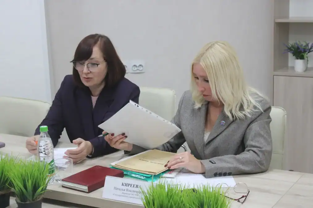 Две женщины изучают бумаги и папку с документами за столом.