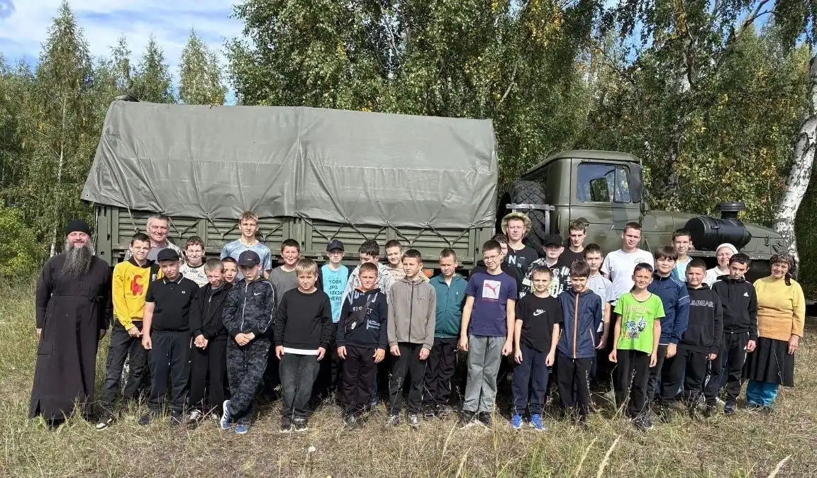 Группа детей и взрослых стоит перед грузовым автомобилем на природе.
