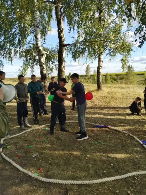 Мальчики участвуют в игре с воздушными шарами на поляне.