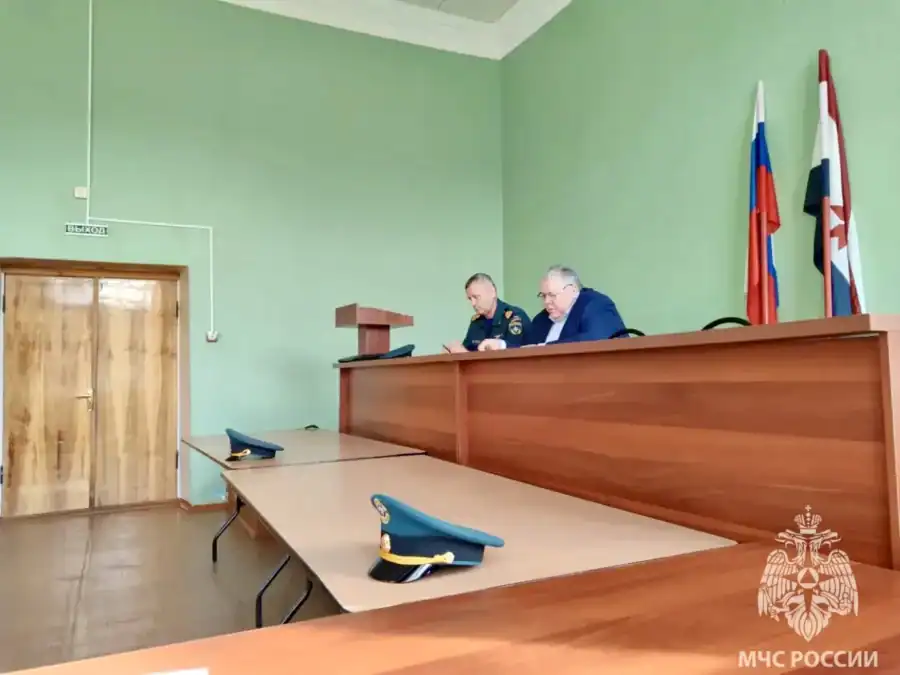 Двое сотрудников в форме сидят за столом президиума в зале.