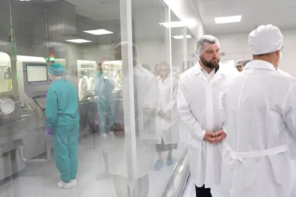 Сотрудники и посетители в белых халатах находятся у производственного оборудования.