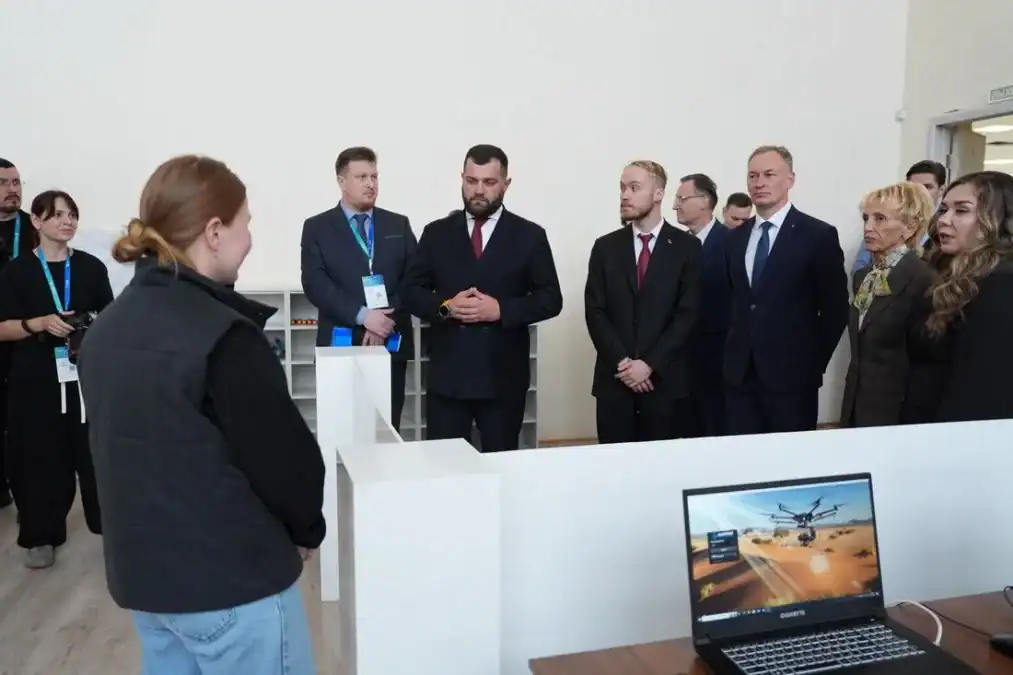 Делегация в деловых костюмах слушает сотрудницу у демонстрационного стенда.