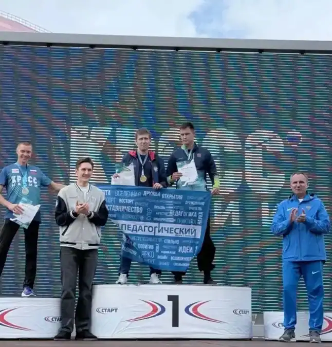 Участники с дипломами стоят на пьедестале перед экраном с баннером «Педагогический».