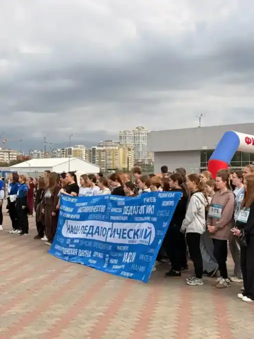 Большая группа участников забега держит синий баннер «Педагогический» на городской площадке.