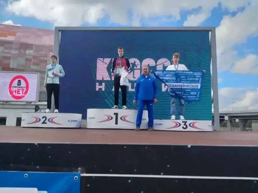 Три спортсмена с дипломами стоят на пьедестале рядом с мужчиной в синем спортивном костюме.