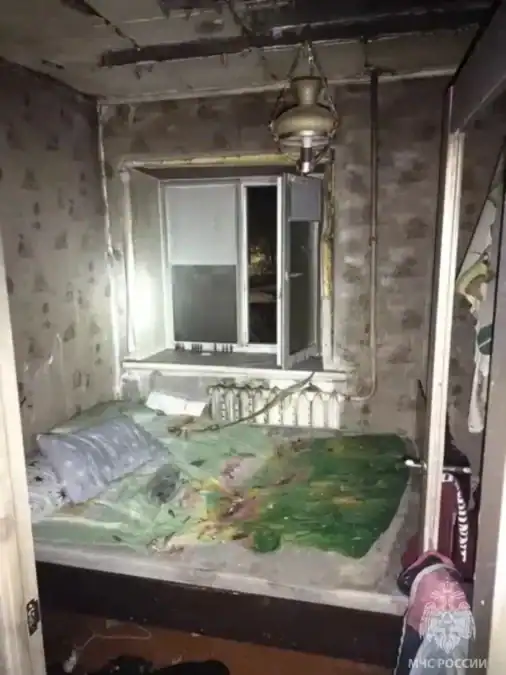 Комната с кроватью, обгоревшими стенами и потолком после пожара.