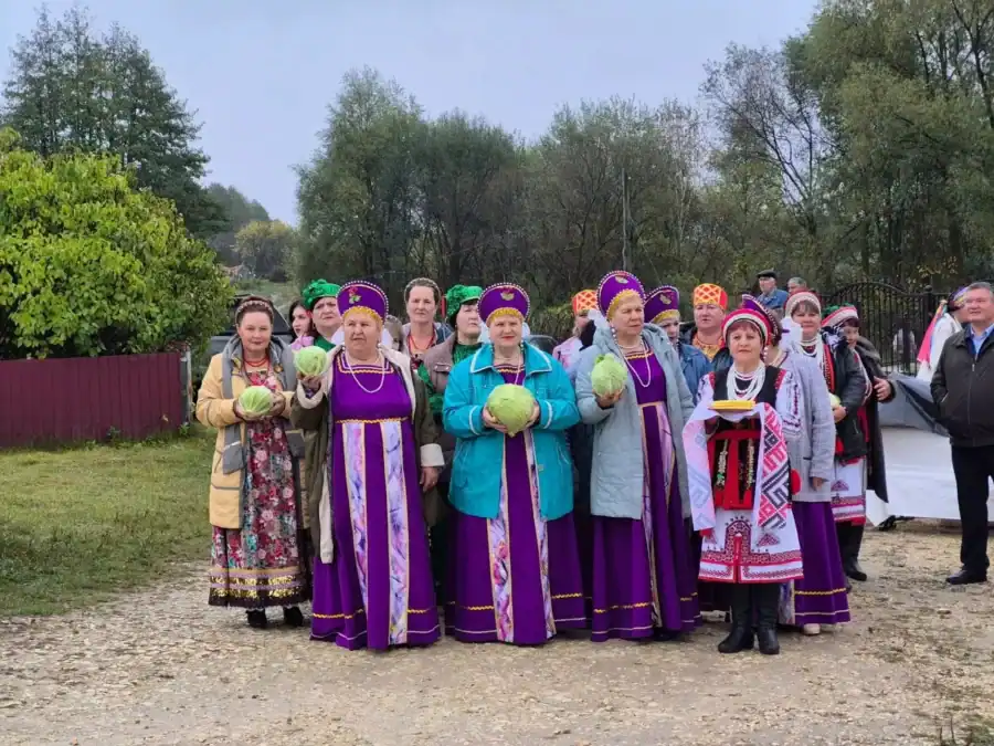 Участницы в национальных костюмах держат кочаны капусты на сельской улице.