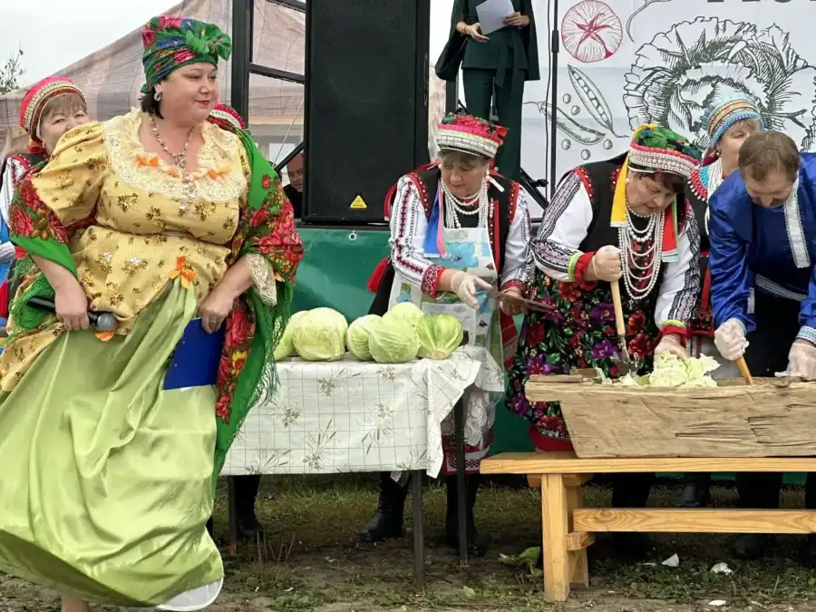 Женщины в национальных костюмах готовят капусту у столов фестивальной площадки.