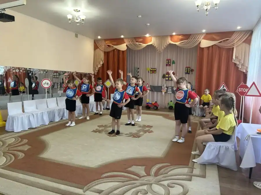Дети с дорожными знаками выступают перед воспитанниками в зале детского сада.