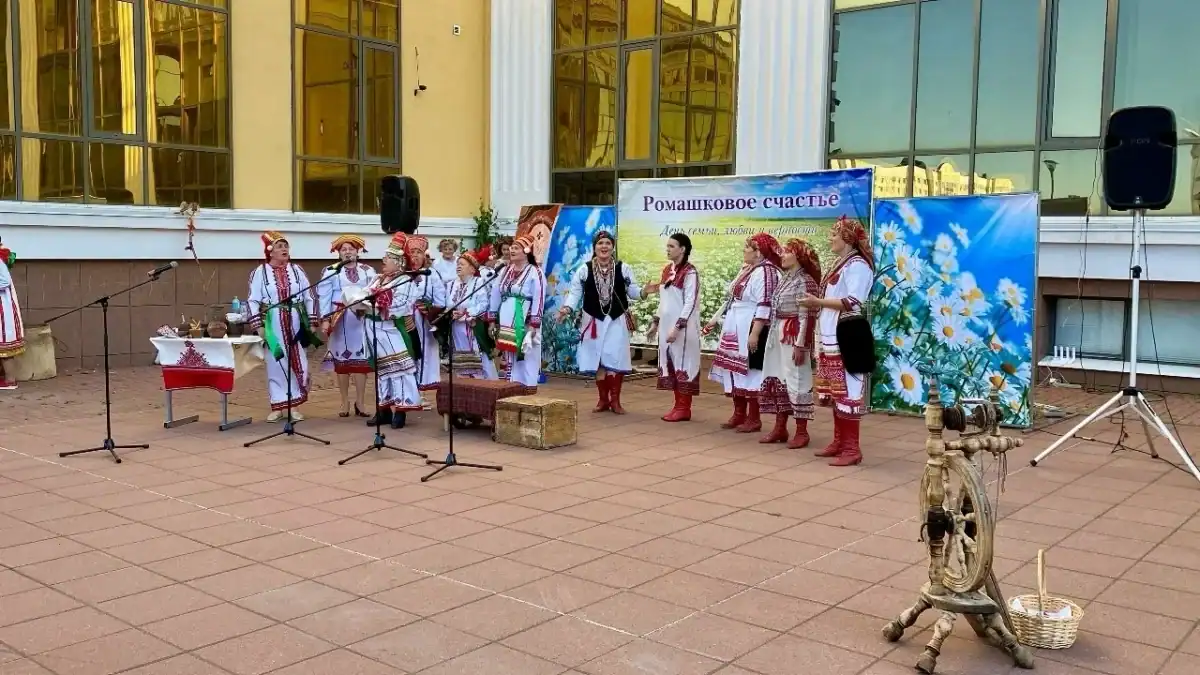 Участники в народных костюмах выступают у микрофонов перед зданием.