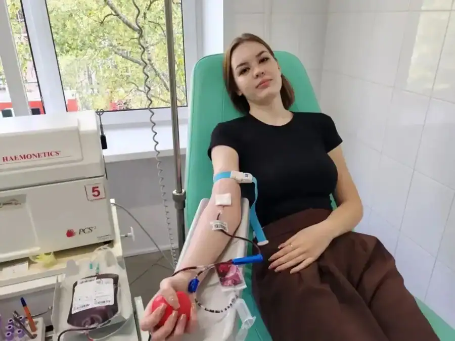 Девушка сдаёт кровь в донорском кресле рядом с контейнером крови.