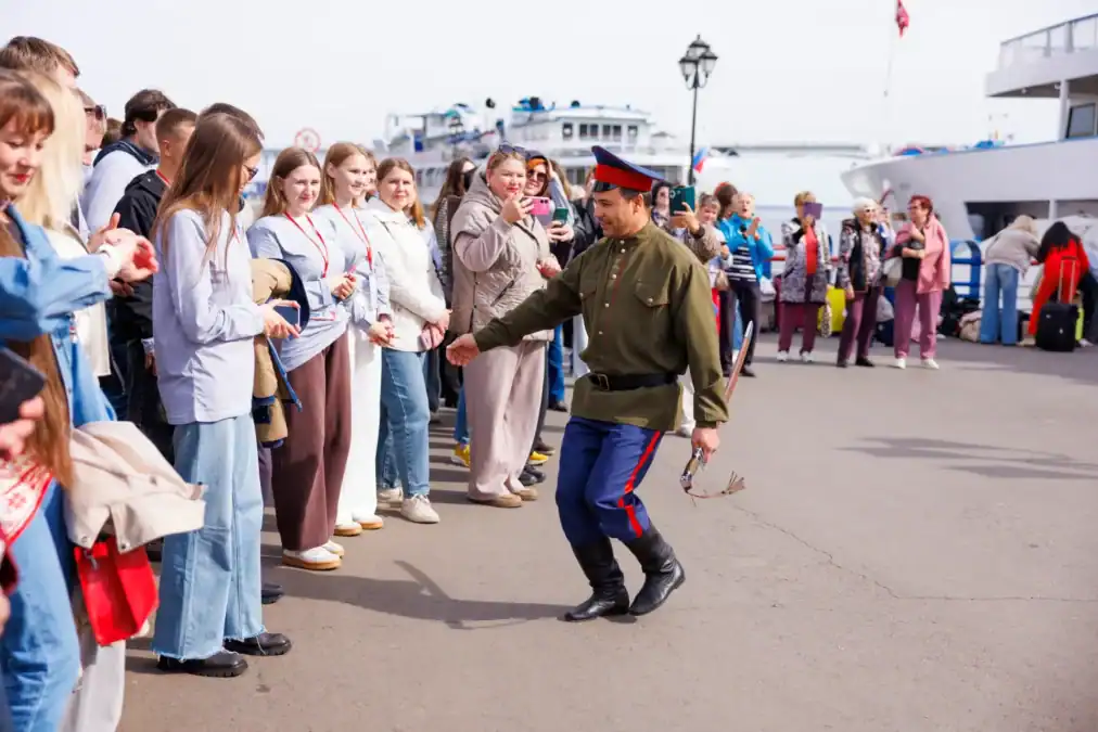 Мужчина в казачьем костюме танцует перед стоящими на причале участниками.