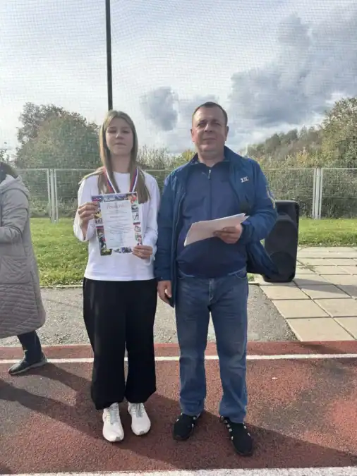 Девушка с медалью показывает грамоту рядом с мужчиной на стадионе.