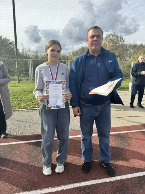 Девушка с медалью и грамотой стоит рядом с мужчиной.