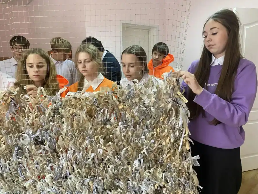 Участницы мастерской вручную закрепляют лоскуты ткани на маскировочной сети.