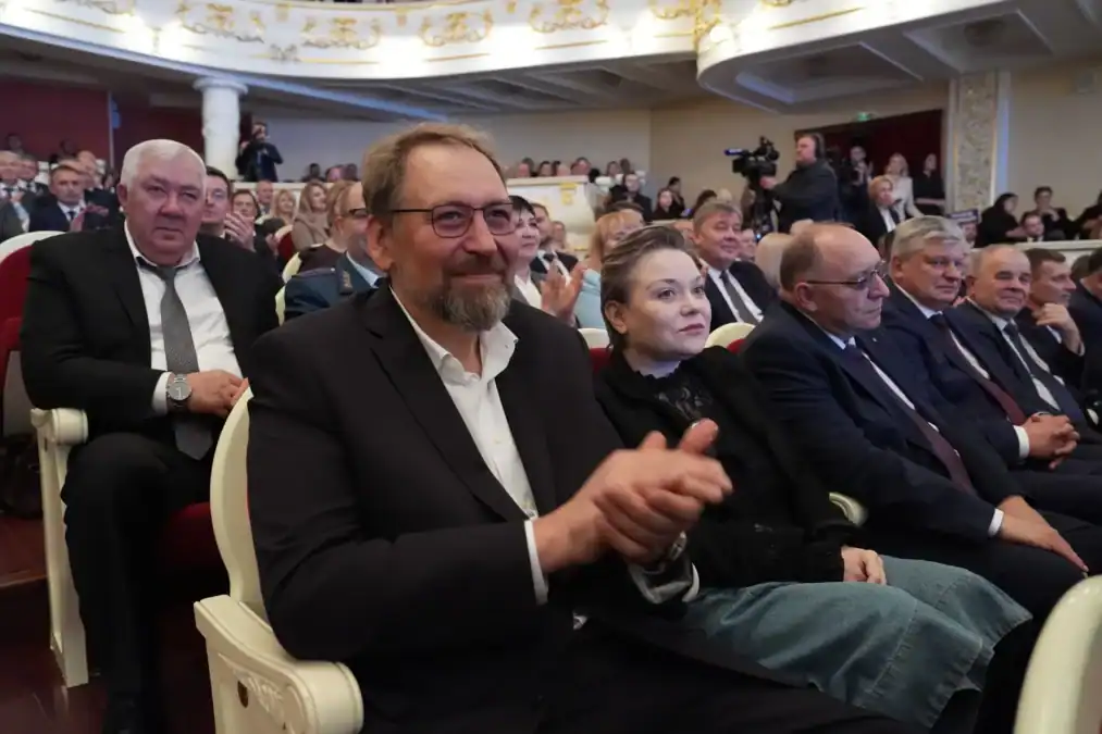 Сидящие в зале мужчины и женщина аплодируют.