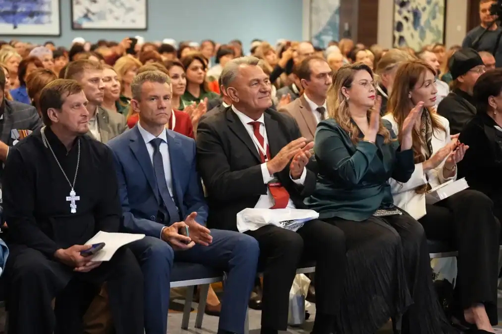 Участники мероприятия сидят в зале и аплодируют.