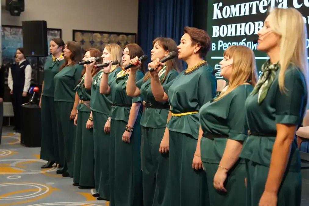 Женщины в зелёных платьях поют на сцене с микрофонами.