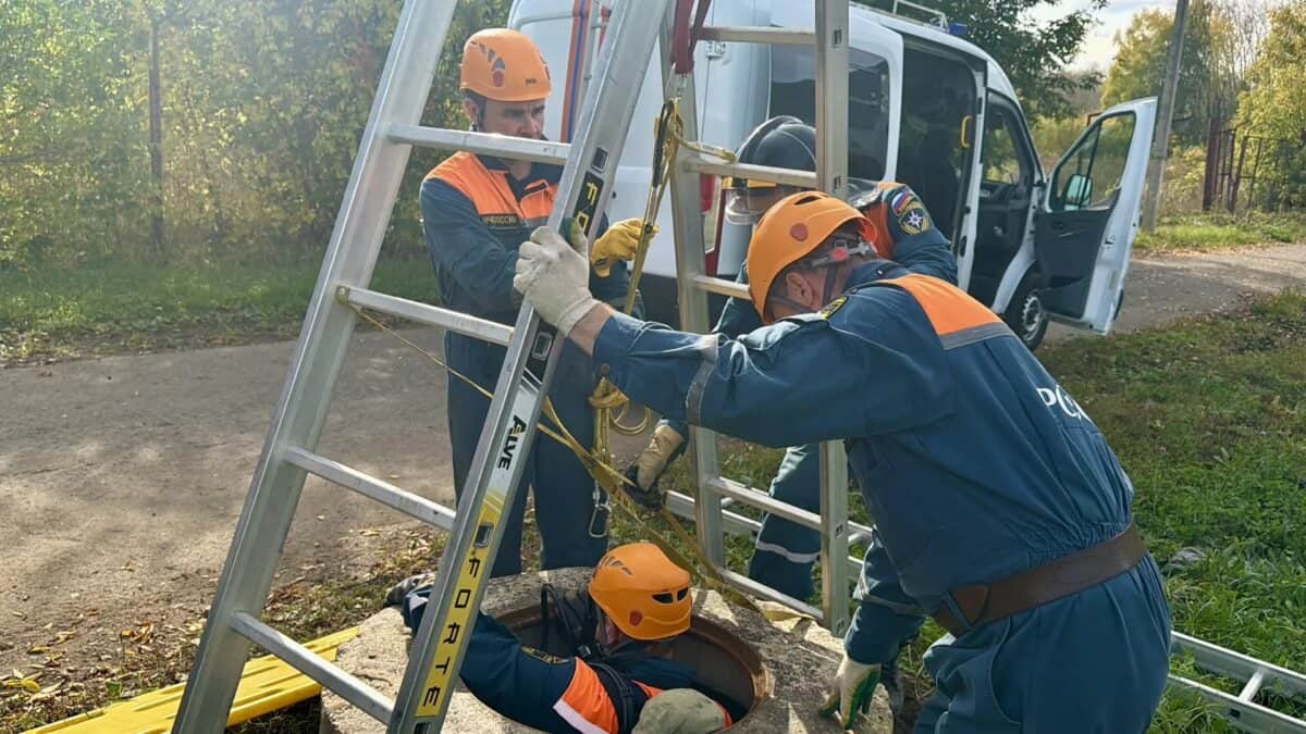 Спасатели в оранжевых касках работают с лестницей и страховочной верёвкой.