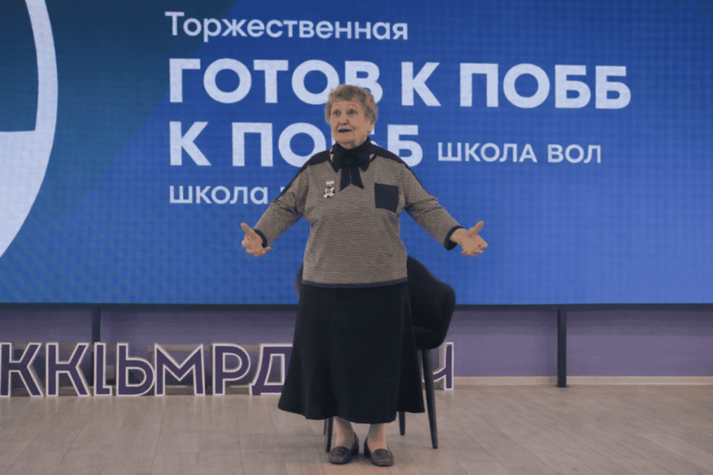 Женщина выступает на сцене перед экраном школы волонтёра.