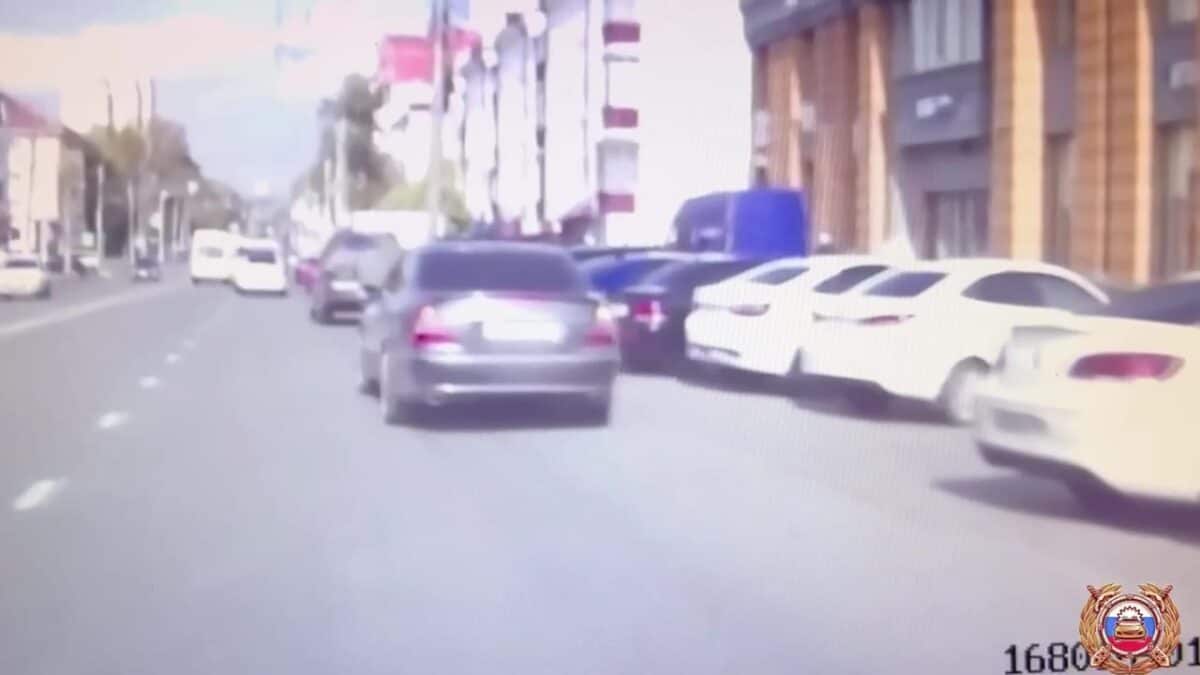 Серебристый автомобиль едет по городской улице рядом с припаркованными машинами.