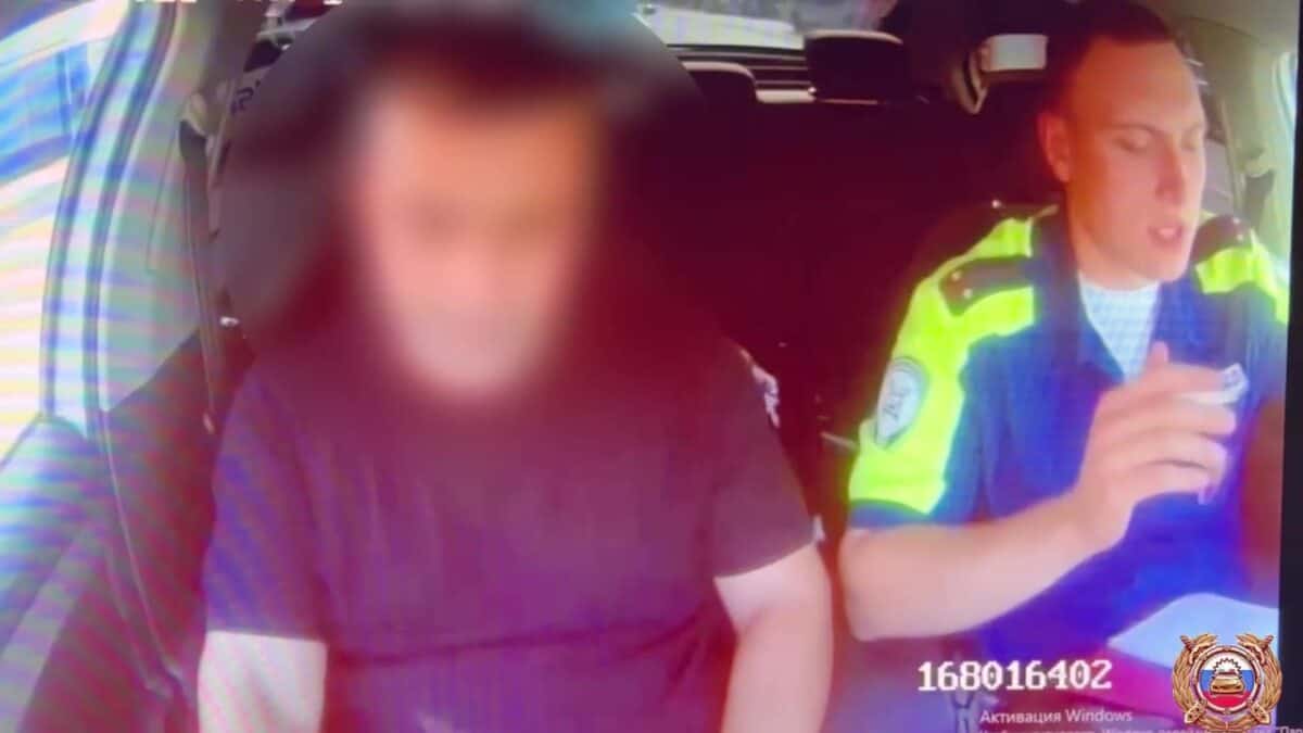Мужчина с размытым лицом сидит в автомобиле рядом с сотрудником полиции.