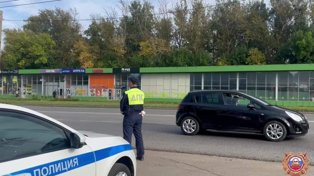 Сотрудник ДПС находится у патрульного автомобиля на обочине городской дороги.